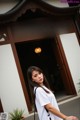 A woman standing in front of a building wearing a white shirt.