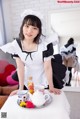 A woman in a maid outfit sitting on a bed with a tray of tea.