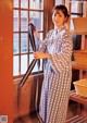 A woman in a blue and white kimono standing in front of a window.