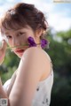 A woman holding a purple flower in front of her face.