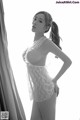 A woman in a white lingerie posing by a window.