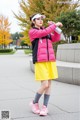 A woman in a pink jacket and yellow skirt holding a water bottle.