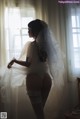 A woman in a wedding dress standing in front of a window.