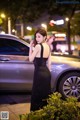 A woman in a black dress standing next to a car.