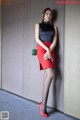 A woman in a black top and red skirt leaning against a wall.