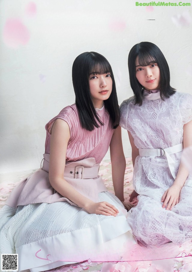 A couple of women sitting next to each other on a bed.